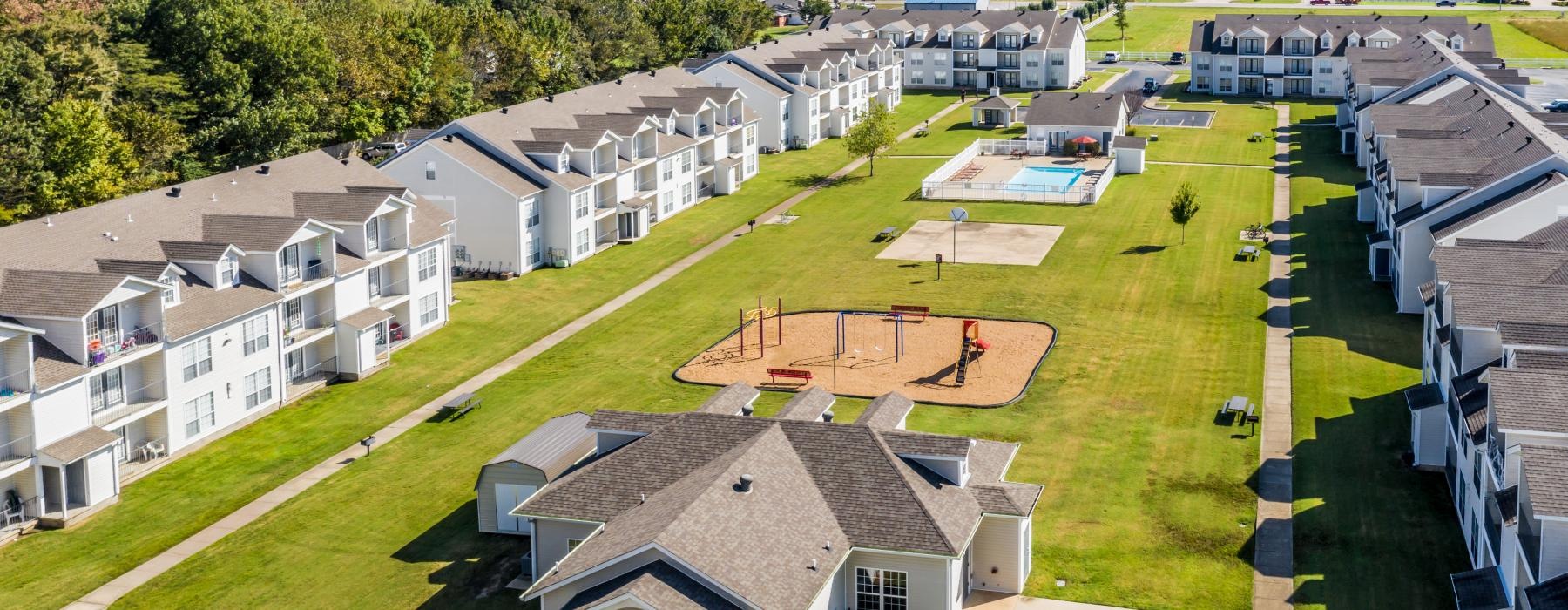 a lawn with a playground and a pool surrounded by buildings
